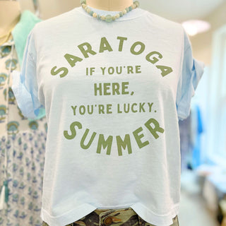 Light blue t-shirt with 'Saratoga Summer - If You're Here, You're Lucky.' text. Styled with beaded necklace and camo pants. Saratoga Springs, NY Boutique